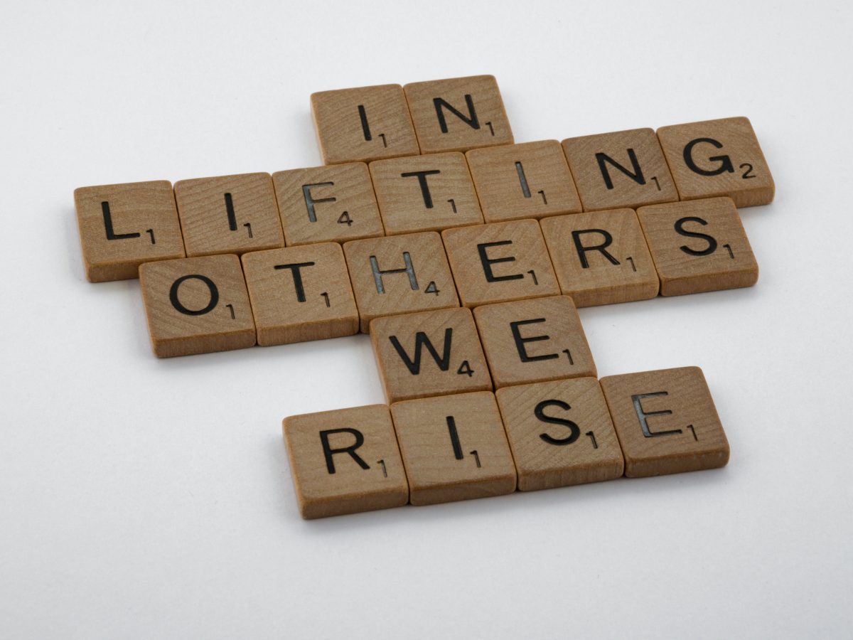 Scrabble tiles spell out "In lifting others, we rise."