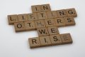 Scrabble tiles spell out "In lifting others, we rise."