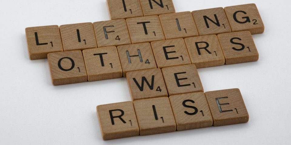 Scrabble tiles spell out "In lifting others, we rise."