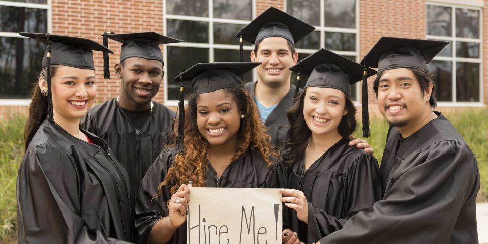 alt=a group of young graduates hold a sign saying hire me